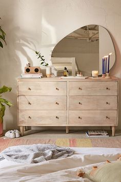 a bedroom with a dresser, mirror and plants on the floor in front of it