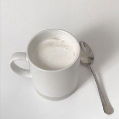 a white coffee cup with a spoon resting on it's side, against a white background