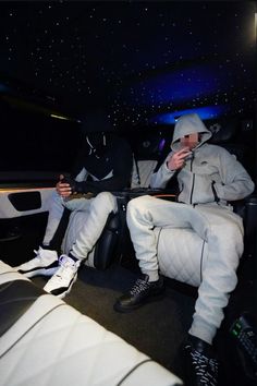 two men sitting in the back of a car with their feet up and one man eating food