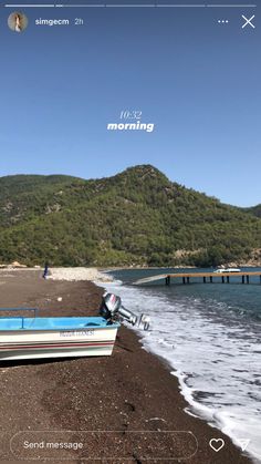 a boat sitting on top of a sandy beach next to the ocean with mountains in the background