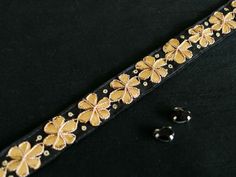 a black belt with gold flowers on it and two earring clips next to it