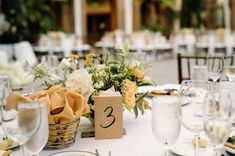 The image shows a close up of a white, yellow & green wedding reception table featuring white and yellow florals, yellow napkins and green accents. 

The table is in the reception space is at the New England Botanic Garden at Tower Hill. Wedding Centerpieces