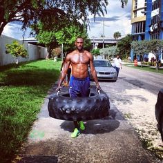 a shirtless man carrying a large tire down the street