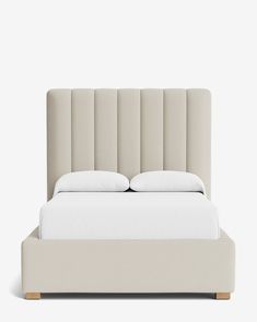 an upholstered bed with white sheets and pillows