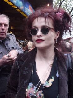 a woman with red hair wearing sunglasses and a black top is standing in front of a crowd