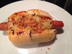 a hot dog on a bun with toppings sitting on top of a white plate