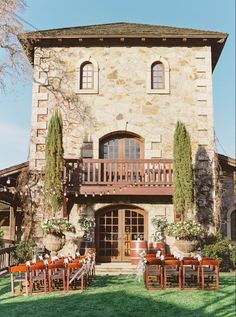 an old stone building with wooden tables and chairs set up in the front lawn area