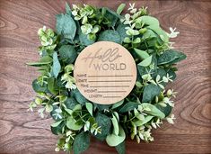 a wreath with the words hello world on it and some green leaves around it, sitting on a wooden surface