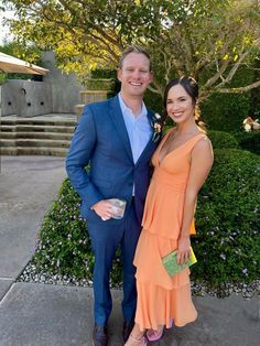 a man and woman standing next to each other in front of some bushes with flowers