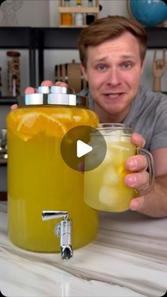 a man is holding a glass with liquid in it next to a large yellow jug