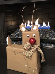 a cardboard box with a reindeer head on it and christmas lights around the top, sitting in front of a fireplace