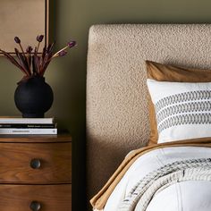 a bedroom with a bed, nightstand and flowers in a vase on top of the headboard