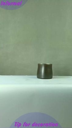 a black cup sitting on top of a white table next to a green and purple wall