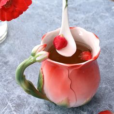 there is a spoon in a tea cup with flowers on the table next to it