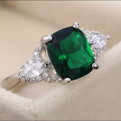 a ring with a green stone surrounded by three white diamonds on top of a cloth