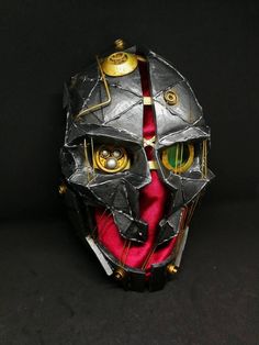 a mask made out of metal and red material with yellow eyes on it's face