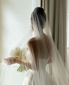 a woman in a wedding dress holding a bouquet of flowers and wearing a long veil