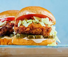 two fried chicken sandwiches with lettuce and tomato slices on a wooden cutting board