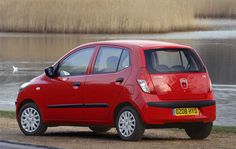 a small red car parked next to a body of water