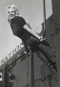 a woman hanging off the side of a train with her legs in the air and smiling