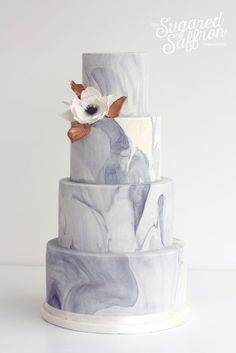 a three tiered cake with white flowers on the top and blue marbled icing