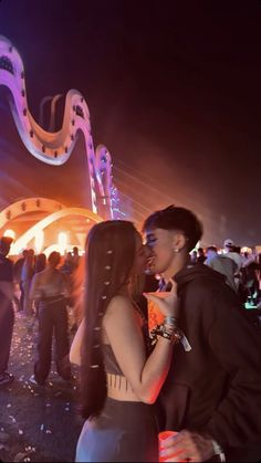 two people standing next to each other in front of an illuminated area at night time