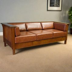 a brown leather couch sitting on top of a carpeted floor next to a potted plant