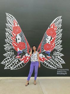 a woman standing in front of a large butterfly painted on the side of a building