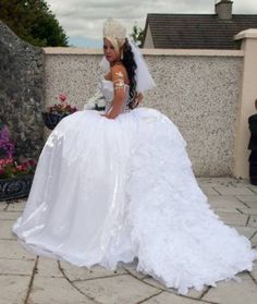 a woman in a white wedding dress sitting on a stone wall next to some flowers