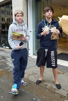 two young men standing next to each other in front of a store window holding food