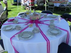 a table set up with plates and cups for a tea party in the grass at an outdoor event