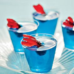 three glasses filled with blue liquid on top of a glass plate and one has red hands sticking out of it