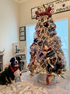 a dog sitting in front of a christmas tree decorated with ribbon and letters on it