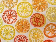 an orange and lemon design on a white fabric with red thread in the center, surrounded by smaller oranges