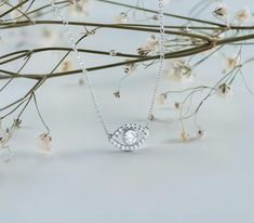 a white diamond necklace sitting on top of a branch with flowers in the foreground