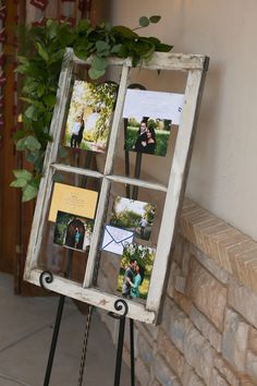 an old window frame with photos on it sitting next to a brick wall and potted plant