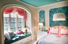 a bedroom with blue and pink wallpaper, white bedding, and window seat