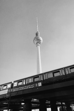 black and white photograph of a train passing under a bridge with the tv tower in the background