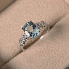 an oval blue topaz and diamond ring sits on a cushioned surface in a box