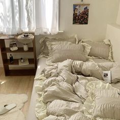 an unmade bed with white sheets and pillows in a bedroom next to a window