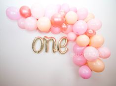 balloons and the word one spelled out in gold letters on a white background with pink and peach colors