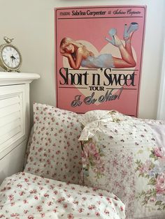 a bed topped with lots of pillows next to a wall mounted clock and a pink sign