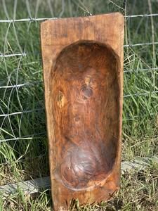 a wooden box sitting in the grass next to a wire fence with a face carved into it