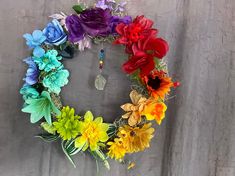 a multicolored flower wreath is hanging on the wall next to a gray curtain