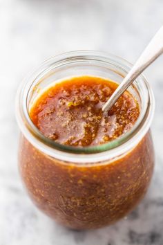 a glass jar filled with sauce on top of a white counter next to a spoon