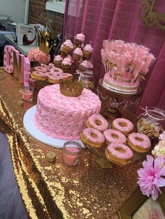 a table topped with pink frosted doughnuts and cake covered in icing