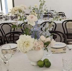 an arrangement of flowers and greenery in a vase on top of a white table cloth