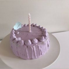 a birthday cake with purple frosting and a single candle on top is sitting on a white plate