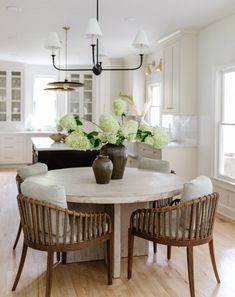 a white table with chairs around it and flowers in vases on the table top