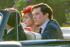 two people sitting in the driver's seat of a car, one wearing a red hat